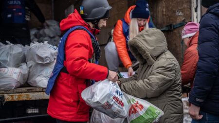 Freiwilliger in roter Jacke und Helm verteilt Hilfspakete in der Ukraine