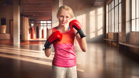 Mädchen in rotem Tanktop und grauer Hose mit roten Boxhandschuhen in einem hellen, großen Trainingsraum mit Boxsäcken und Fenstern