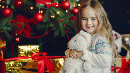 Mädchen mit Kuscheltier vor Weihnachtsbaum und Geschenken