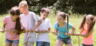 Fünf Kinder ziehen an einem Seil im Freien. Sie stehen auf einer Wiese und lachen.