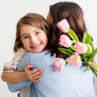 Kind umarmt eine Frau, die einen Strauß rosa Tulpen hält