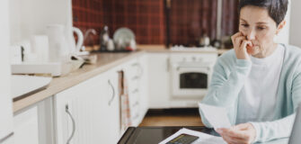 Eine Person sitzt am Küchentisch und betrachtet sorgenvoll eine Rechnung.