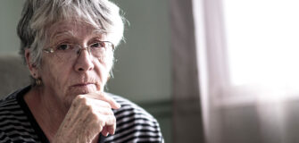 Eine ältere Frau sitzt nachdenklich am Fenster – viele Pensionistinnen sind von Altersarmut betroffen.