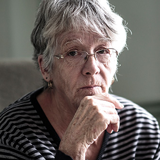 Eine ältere Frau sitzt nachdenklich am Fenster – viele Pensionistinnen sind von Altersarmut betroffen.