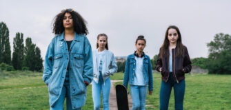 Vier Jugendliche gehen gemeinsam auf einem Weg durch eine Grünfläche, im Hintergrund sind Bäume und eine offene Landschaft zu sehen.