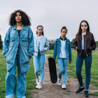 Vier Jugendliche gehen gemeinsam auf einem Weg durch eine Grünfläche, im Hintergrund sind Bäume und eine offene Landschaft zu sehen.