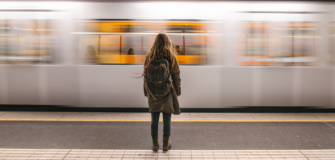 Person steht auf einem Bahnsteig und blickt auf eine vorbeifahrende U-Bahn in einer Station.