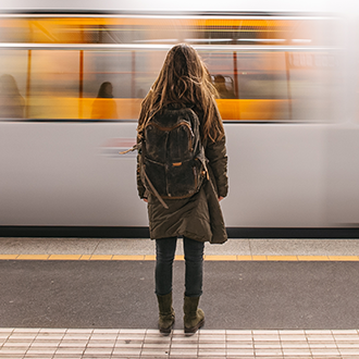 Person steht auf einem Bahnsteig und blickt auf eine vorbeifahrende U-Bahn in einer Station.