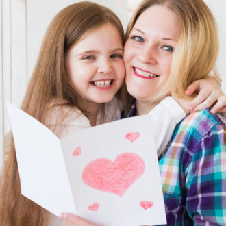 Herzensgeschenk zum Muttertag: Kind hält eine selbstgemachte Karte mit großen und kleinen Herzen vor sich und umarmt eine Frau