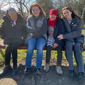Zwei Mitarbeiterinnen sitzen mit zwei älteren Frauen im Freien auf einer Schaukel in der Region Odessa.