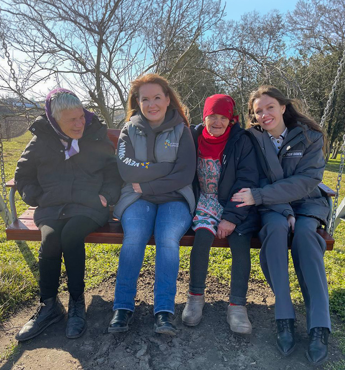 Zwei Mitarbeiterinnen sitzen mit zwei älteren Frauen im Freien auf einer Schaukel in der Region Odessa.
