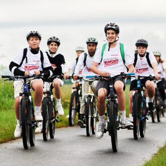 Kinder und Jugendliche fahren gemeinsam mit Fahrrädern bei der Tour de Chance 2026 der Volkshilfe über eine Straße im ländlichen Raum