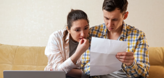 Zwei Personen sitzen auf einem Sofa und betrachten gemeinsam ein Dokument. Vor ihnen stehen ein Laptop und weitere Unterlagen auf einem Tisch.