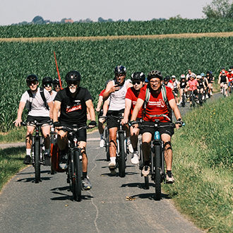 Lange Kolonne von Radfahrer*innen der Tour de Chance auf einem Radweg zwischen Feldern im Südburgenland. Gemeinsam setzen sie ein Zeichen gegen Kinderarmut in Österreich.
