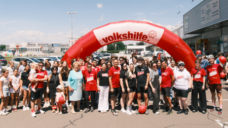 Teilnehmer*innen der Tour de Chance versammeln sich für ein Gruppenfoto unter einem Volkshilfe-Bogen beim Abschluss in Güssing.