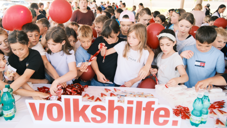 Kinder versammeln sich um einen Informationstisch der Volkshilfe und nehmen Materialien entgegen.