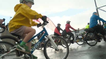 Kind auf einem Fahrrad bei der Kidical Mass und der Tour de Chance 2026 in Wien, im Hintergrund Volkshilfe-Radfahrer*innen mit Fahne.