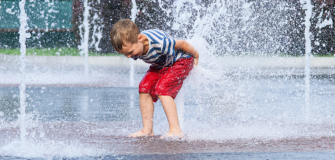 Ein Kind spielt an einem heißen Sommertag zwischen Wasserfontänen auf einem öffentlichen Platz.