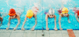 Mehrere Kinder mit bunten Schwimmhauben üben gemeinsam in einem Schwimmbecken während eines Schwimmkurses.