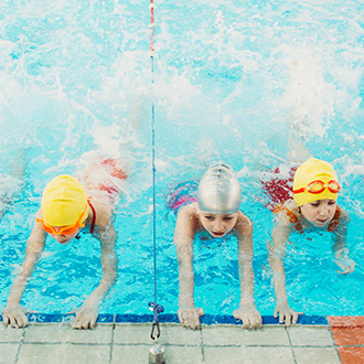 Mehrere Kinder mit bunten Schwimmhauben üben gemeinsam in einem Schwimmbecken während eines Schwimmkurses.