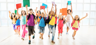 Eine Gruppe von Schulkindern läuft mit Schultaschen und bunten Heften durch einen hellen Raum auf die Kamera zu.