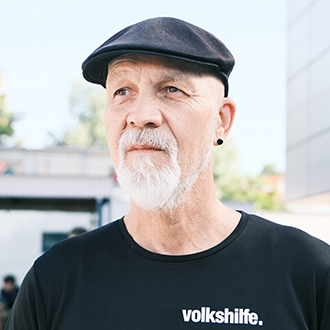 Erich Fenninger steht im Freien vor einem Gebäude und trägt ein schwarzes T-Shirt mit Volkshilfe-Logo.