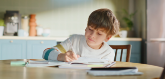 Kind sitzt allein am Tisch und schreibt in ein Schulheft.
