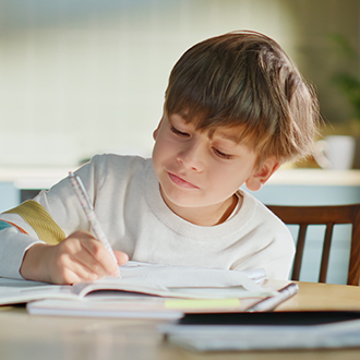 Kind sitzt allein am Tisch und schreibt in ein Schulheft.