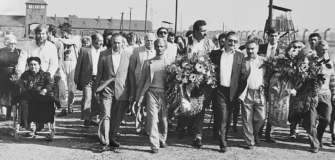 Teilnehmende einer Gedenkveranstaltung gehen mit Kränzen auf dem Gelände des ehemaligen Konzentrationslagers Auschwitz-Birkenau.