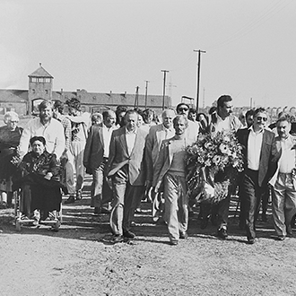 Teilnehmende einer Gedenkveranstaltung gehen mit Kränzen auf dem Gelände des ehemaligen Konzentrationslagers Auschwitz-Birkenau.