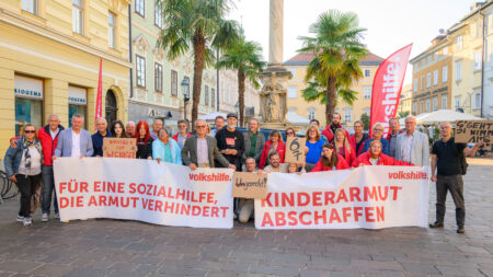 Teilnehmer*innen am Alten Platz in Klagenfurt halten Transparente mit den Aufschriften „Für eine Sozialhilfe, die Armut verhindert“ und „Kinderarmut abschaffen“.