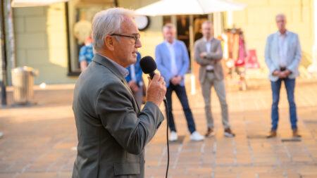 Volkshilfe Kärnten-Präsident Ewald Wiedenbauer spricht am Alten Platz in Klagenfurt in ein Mikrofon. Im Hintergrund stehen Zuhörer*innen.