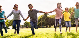 Eine Gruppe von Kindern läuft Hand in Hand gemeinsam über eine Wiese – Symbol für Teilhabe und gleiche Chancen.