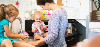 Eine Frau mit zwei Kindern am Spülbecken in einer Küche beim gemeinsamen Abwaschen.
