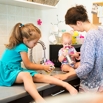 Eine Frau mit zwei Kindern am Spülbecken in einer Küche beim gemeinsamen Abwaschen.