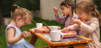 Drei Kinder sitzen an einem Holztisch im Garten und essen gemeinsam.