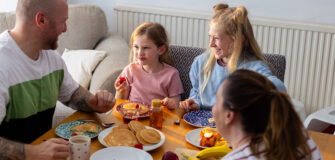 Familie mit zwei Kindern beim gemeinsamen Frühstück mit Obst und Pfannkuchen zu Hause.