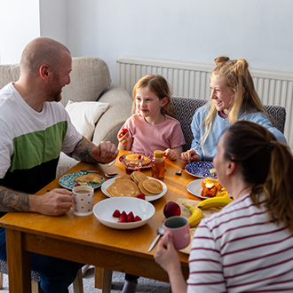 Familie mit zwei Kindern beim gemeinsamen Frühstück mit Obst und Pfannkuchen zu Hause.