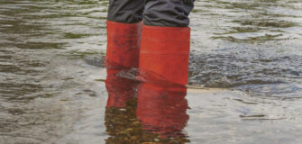 Eine Person steht mit roten Gummistiefeln im Wasser.